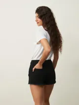 Short de denim negro de tiro alto, con bolsillos delanteros y traseros, y terminaciones deshilachadas en las piernas.