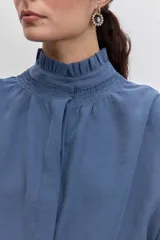 Camisa azul de manga larga con cuello alto fruncido y puños elásticos.