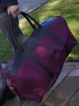 Bolso de viaje tipo duffel de lona negra con detalles en cuero tostado, asas de mano y correa ajustable para el hombro.