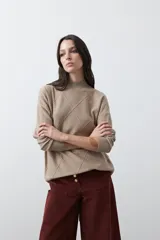 Polera de tejido de punto color beige, con cuello alto y diseño de rombos en relieve en la parte frontal. Presenta un calce relajado con terminaciones en rib en cuello, puños y ruedo.