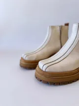 Botas Chelsea de cuero color crudo con elástico lateral, suela track color caramelo y tirador trasero de cuero con textura croco color marrón.