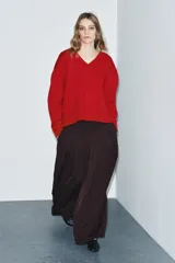 Pantalón de tiro medio con pierna ancha, confeccionado en tela de color marrón oscuro. Presenta pliegues frontales decorativos, bolsillos laterales ocultos en la costura y cierre frontal con cremallera, botón y ganchos metálicos.