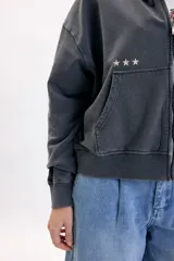 Campera deportiva con capucha y cierre frontal, de color gris con efecto acid wash. Presenta bolsillos tipo canguro, estampa con la inscripción 'Creative Lab' y detalles de pequeñas estrellas en el pecho.