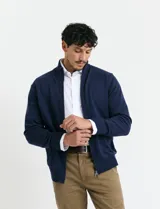 Cardigan de punto gris con cuello alto, cierre frontal de metal con doble cursor y bolsillos laterales. Presenta puños y cuello en tejido canalé.
