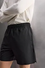 Pantalones cortos deportivos color marrón rojizo, confeccionados en tejido técnico ligero y elástico. Presentan cintura elástica ajustable con cordón interior, bolsillos frontales y un bolsillo trasero con cierre de cremallera. Los laterales tienen perforaciones para transpirabilidad y aberturas laterales en el bajo.