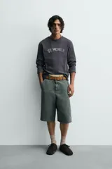 Camiseta de manga larga, corte ajustado (muscle fit), color gris oscuro con efecto lavado. Presenta un estampado frontal desgastado con el texto curvo "ST MONICA" en color plateado o gris claro.