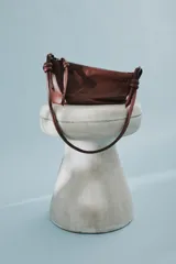 Cartera bandolera de cuero marrón con forma relajada, diseño de costuras curvas y detalles de nudos hechos a mano en las asas.
