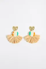 Aros colgantes con forma de abanico, hechos con rafia color beige. Cuentan con un dije circular de cerámica blanca con detalles en verde y naranja, y un dije superior en forma de corazón dorado.