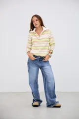 Sweater de punto con cuello alto y cierre frontal, de manga larga y diseño holgado. Presenta un patrón de ondas en colores blanco, beige y verde lima.