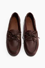 Zapatos náuticos de cuero color marrón con cordones frontales, ojales metálicos dorados y costura de mocasín en la puntera.