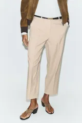 Pantalón tobillero de corte recto en color beige, con detalle de nervio delantero marcado. Incluye cinturón fino, bolsillos delanteros y cierre frontal con cremallera, botón interior y gancho.