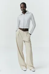 Pantalón gris de tiro alto con bolsillos delanteros y traseros, detalle de pliegues frontales y cierre frontal con cremallera y botón.