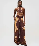 Blusa halter color marrón de viscosa, con diseño sin mangas, cuello halter con atadura posterior y estampa tropical inspirada en pañuelo con detalles en tonos dorados y naranjas.