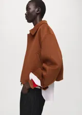 Chaqueta marrón de corte corto y diseño estructurado, con cuello solapa, cierre frontal de cremallera y mangas largas con puños anchos.