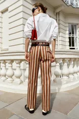 Pantalón de tiro alto y pernera recta con estampado de rayas verticales en tonos azul, marrón y beige. Incluye un cinturón delgado de color marrón oscuro con hebilla metálica dorada.