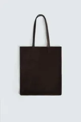Bolso tipo shopper de diseño minimalista, confeccionado en piel con acabado de serraje. Cuenta con dos asas largas de mano y un compartimento principal espacioso con bolsillo interior con cierre.