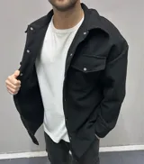 Chaqueta negra de paño con cuello clásico, cierre frontal con botones a presión, dos bolsillos de parche en el pecho y corte holgado.