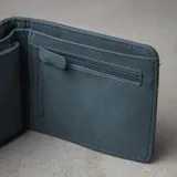 Billetera plegable de eco cuero azul, con múltiples compartimentos para tarjetas, monedero con cierre, tarjetero con visor y dos espacios para billetes. Presenta líneas de pespunte decorativas en la parte superior y el logo de la marca grabado en la esquina inferior.
