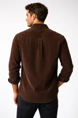 Camisa de pana color marrón, de manga larga, con cuello clásico abotonado y cierre frontal con botones.