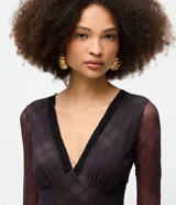 Body de tul negro con transparencia, manga larga y escote en V profundo con detalle de encaje en el borde. Presenta un diseño ajustado al cuerpo con cierre de broches a presión en la parte inferior.