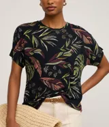 Blusa de manga corta y escote redondo, confeccionada en viscolycra con un estampado de hojas tropicales en tonos verdes, rojizos y crema sobre fondo negro.