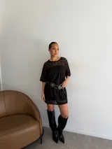 Remerón de encaje negro con mangas cortas y cuello redondo, acompañado de un vestido strapless interior corto en el mismo tono.