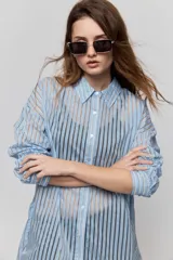 Camisa de rayas de calce relajado, confeccionada en tejido liviano y semitransparente, con cuello clásico, cierre frontal con botones, mangas largas con puños y hombros caídos.