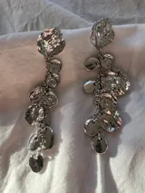 Par de aros largos plateados con cierre de tuerca. Presentan un diseño colgante con diferentes piezas irregulares y circulares unidas por pequeñas cadenas.