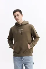 Canguro oversize color verde militar, con capucha ajustable, bolsillo frontal tipo canguro y estampa sutil en el pecho. Presenta puños y ruedo acanalados.