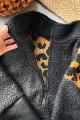 Buzo de corderito con diseño combinado, cuerpo principal en color negro y panel superior trasero en estampado animal print. Presenta cuello alto y cierre frontal.