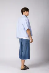 Camisa de manga corta de corte boxy, confeccionada en popelina a rayas celestes y blancas. Presenta cuello camisero clásico, cierre frontal con botones y estampado tipográfico en el pecho.
