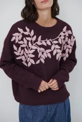 Buzo de tejido de punto en color beige, con cuello redondo y mangas largas. Presenta un delicado bordado de ramas y hojas en color crema en la parte superior del frente.