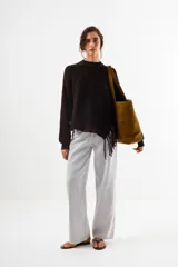 Sweater negro de tejido acanalado, con cuello redondo y un detalle asimétrico en el ruedo inferior con flecos largos.