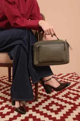 Bandolera de diseño rectangular en color suela, confeccionada en material sintético. Cuenta con un asa superior fija, correa larga ajustable y extraíble, y dos bolsillos frontales con cierre metálico, uno de ellos con diseño superpuesto. Presenta el logo de la marca grabado en el frente.