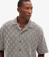 Camisa de manga corta Marfinno con corte boxy, cuello bowling y cierre frontal abotonado. Confeccionada en tejido texturizado con diseño geométrico de cuadros.