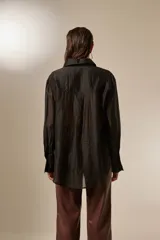 Camisa negra de lyocell, manga larga, con cuello camisero y botones frontales. La prenda está adornada con pequeños apliques de strass distribuidos por toda la tela.