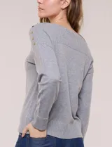 Buzo de punto fino color gris, de calce relajado, escote redondo amplio y canesú con textura acanalada. Cuenta con apliques de tachas metálicas doradas en la línea del hombro, mangas largas de hombro caído y puños y ruedo acanalados.