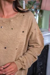 Sweater de corte oversize color beige, confeccionado en algodón. Presenta un diseño holgado con cuello redondo, puños y ruedo acanalados, decorado con múltiples apliques metálicos circulares en tonos dorados y plateados distribuidos por toda la prenda.