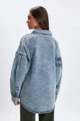 Sobrecamisa de jean en tono celeste con efecto lavado, corte oversize, cuello clásico, cierre frontal con botones metálicos y mangas largas con detalle de frunces en los hombros.