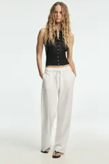 Pantalón blanco de tiro medio con pierna ancha y tejido que contiene lino. Presenta cintura con trabillas y un cinturón ajustable con lazada del mismo tejido. Cierre frontal con cremallera y botón.