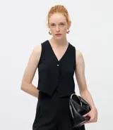 Chaleco femenino de corte sastre confeccionado en tejido punto roma, con escote en V y cierre frontal mediante botones. Presenta un diseño estructurado sin mangas, ideal para superposiciones.