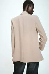 Blazer de corte recto y diseño estructurado en color beige, con cuello solapa, manga larga y cierre frontal con un solo botón. Cuenta con bolsillos delanteros con solapa y forro interior en color negro.