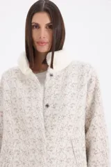 Saco de paño con textura jaspeada en tonos beige y visón, con cuello redondo y cierre frontal con botones a presión. Presenta mangas largas con puños tejidos en color crema y detalles de piel sintética en el cuello.