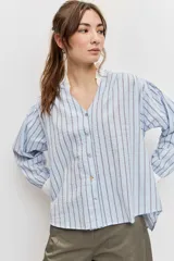 Camisa de rayas celestes y marrones, de corte holgado y manga larga, con cuello en V y detalles blancos en el cuello y los puños.