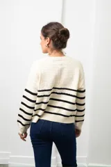 Saco de punto con cierre frontal, diseño a rayas horizontales negras sobre base color crema, de manga larga y calce holgado.