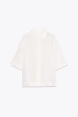 Camisa blanca de manga corta con cuello solapa y cierre frontal de botones. Presenta un corte recto y holgado.