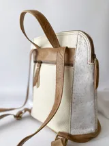 Mochila de cuero color beige y blanco, con detalles laterales texturizados, bolsillos frontales verticales con cierre y asas ajustables.