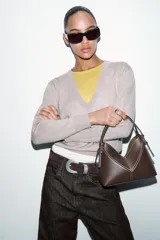 Bolso tipo mini shopper de estructura rígida en color crudo, con detalles de costuras en contraste y ribetes en color marrón oscuro. Cuenta con un asa de mano fija y cierre superior.