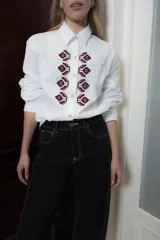 Camisa de algodón con corte clásico, cuello camisero y mangas largas con puños abotonados. Presenta un bordado geométrico en color bordó en la parte frontal y detalle de frunce en la espalda.