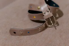 Cinturón de cuero sintético negro adornado con pequeños cristales de colores y tachas metálicas.